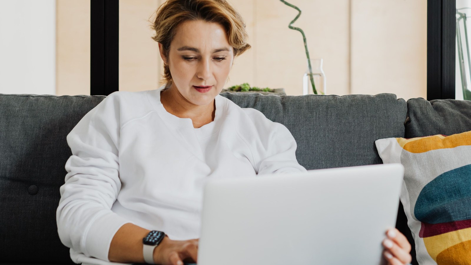 A woman sitting on a couch at home with a laptop, working through a consultation call