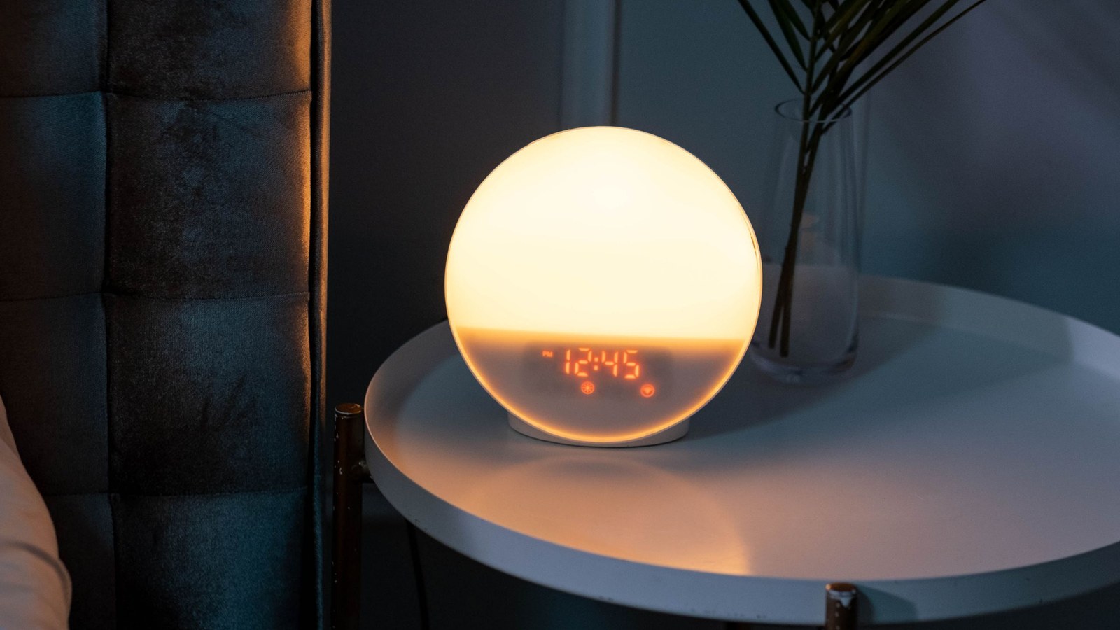 A softly glowing bedside clock reading 12:45 on a night table in a dark, quiet bedroom