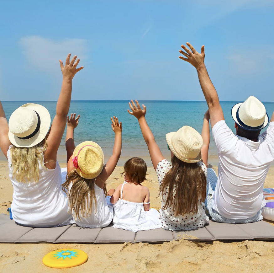 Family with children sitting on beach boardwalk with arms raised celebrating summer vacation