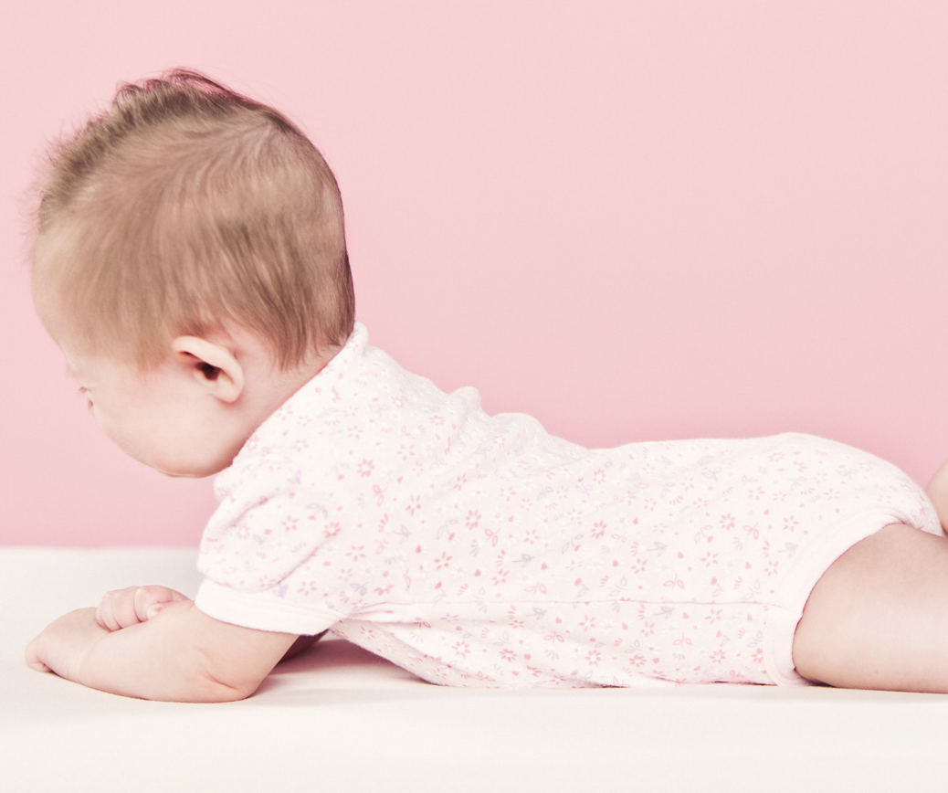 Baby in pink outfit lying on their tummy against pink background