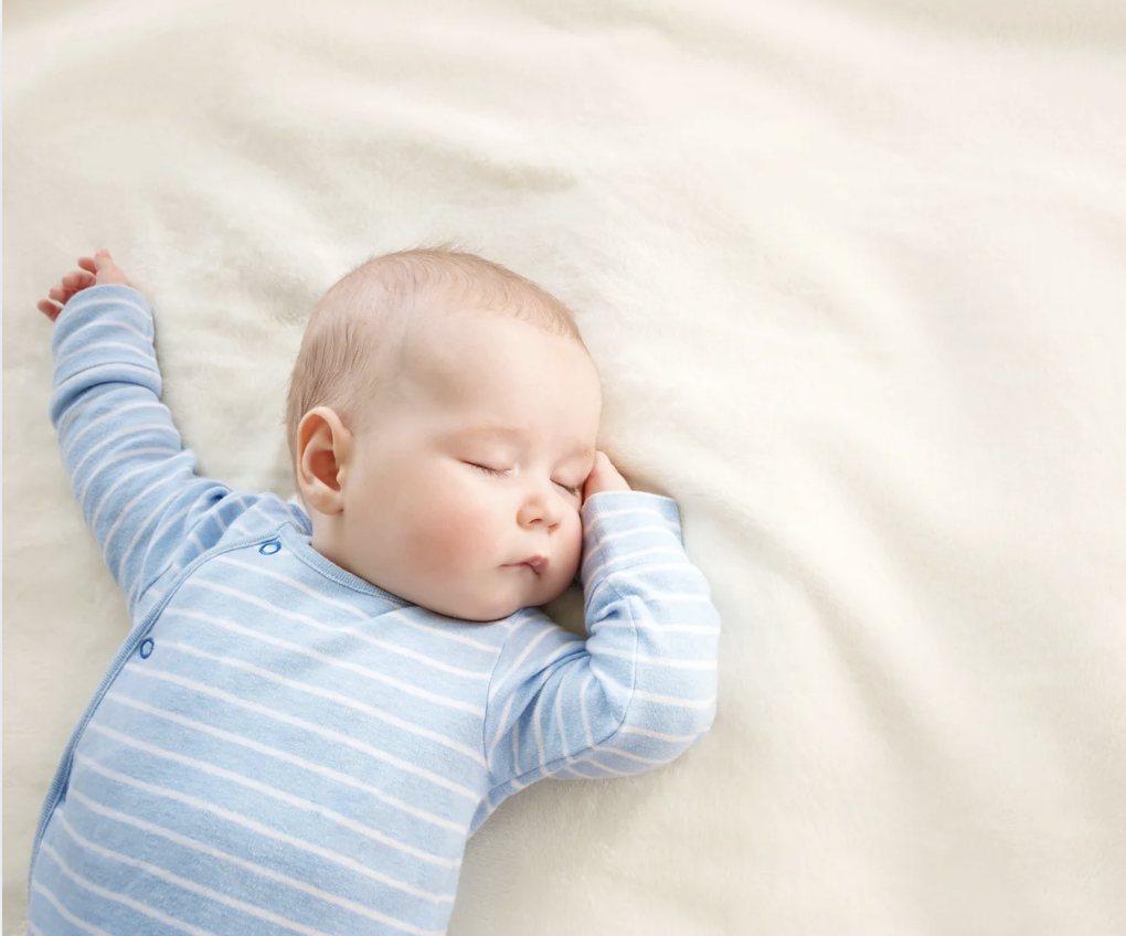 Peacefully sleeping baby in blue striped outfit on white bedding