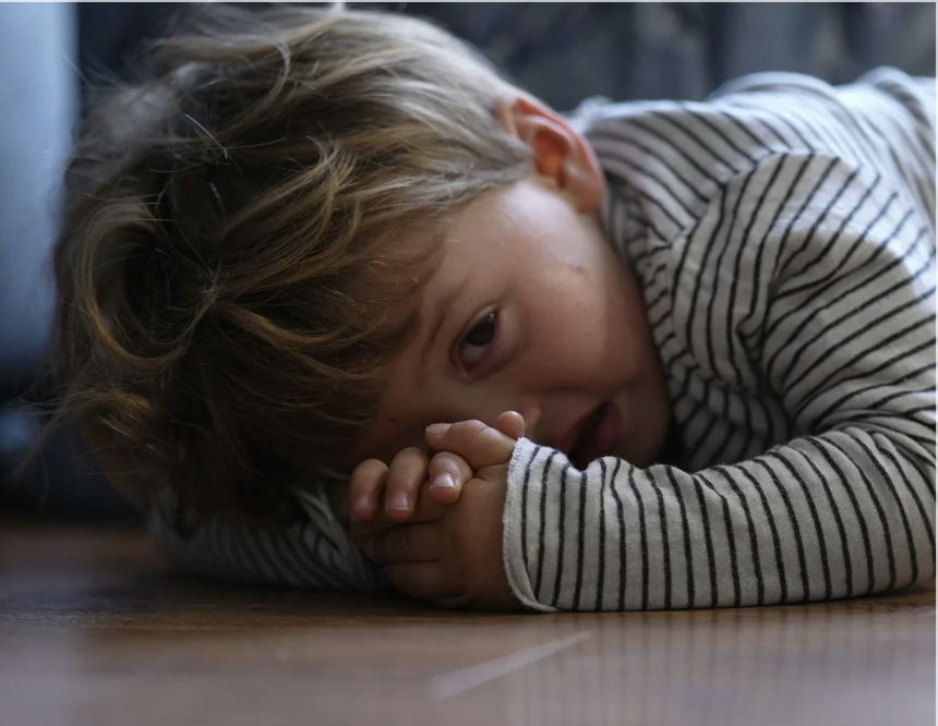 Child lying on wooden floor with striped shirt
