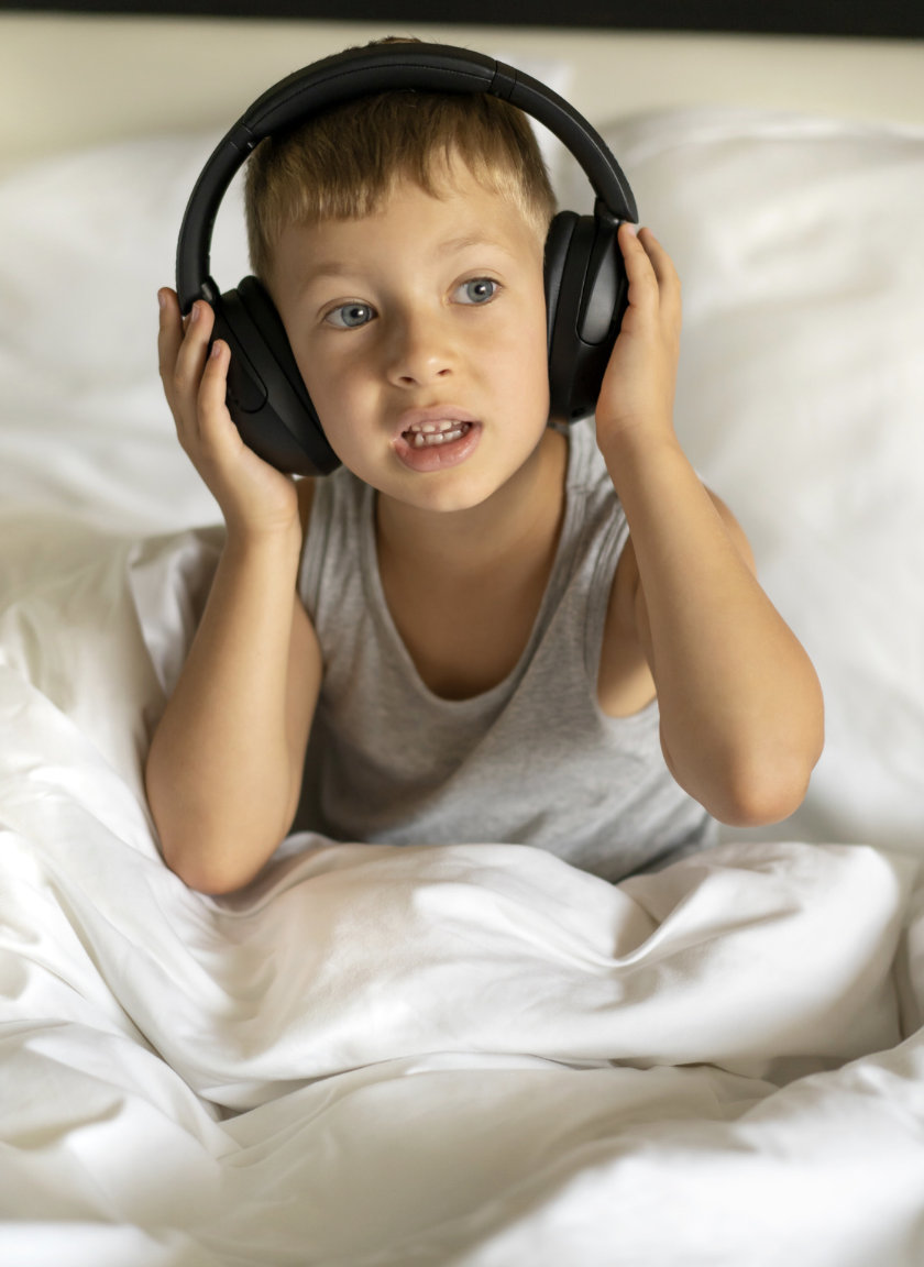 Child wearing headphones in bed under soft white sheets at bedtime